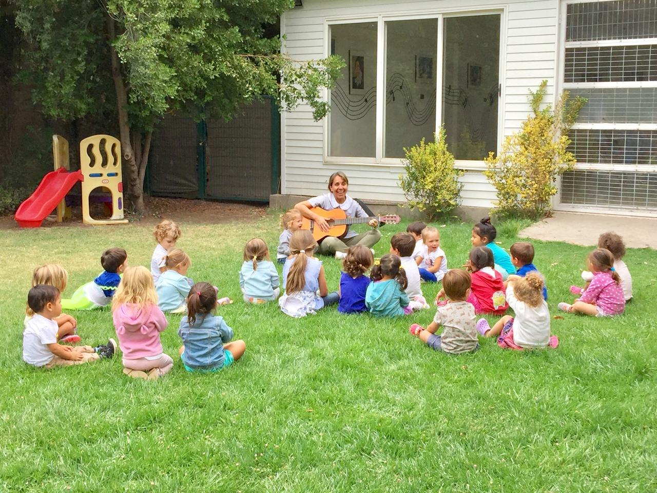 Miss tocando guitarra para un grupo grande de niños en el pasto